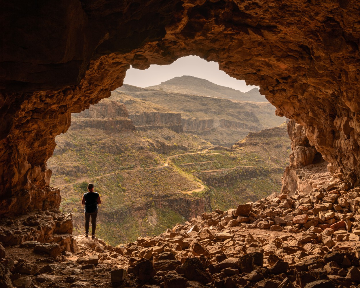 Person steht am Eingang einer Höhle und blickt über eine felsige Schluchtlandschaft.